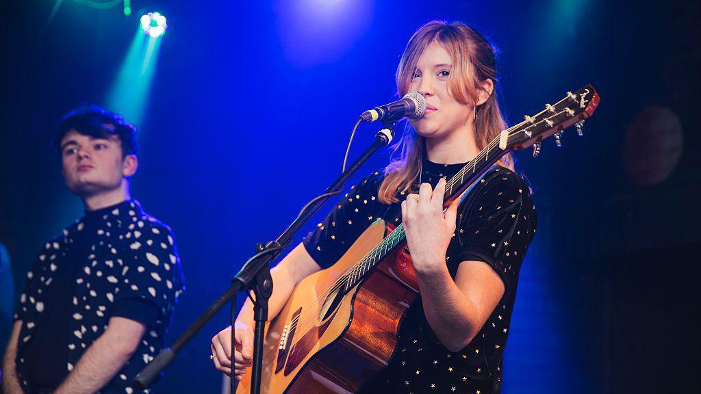 Cara Hammond performing with an acoustic guitar.