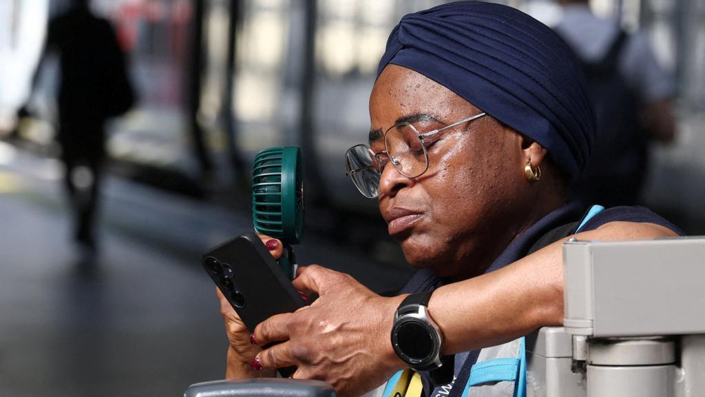 A railway worker uses an electric fan to cool herself down on a train platform in London.