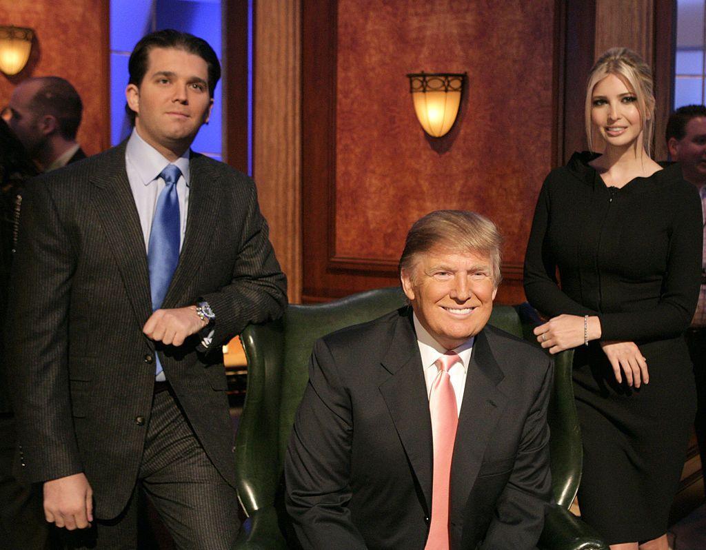 A smiling, seated Donald Trump is flanked by his son Donald Trump Jr. and  his daughter Ivanka Trump for a publicity shot for the season 6 finale of The Apprentice.