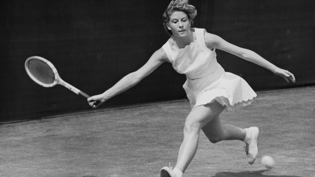 Pericoli returns a forehand serve in a white dress, mid movement