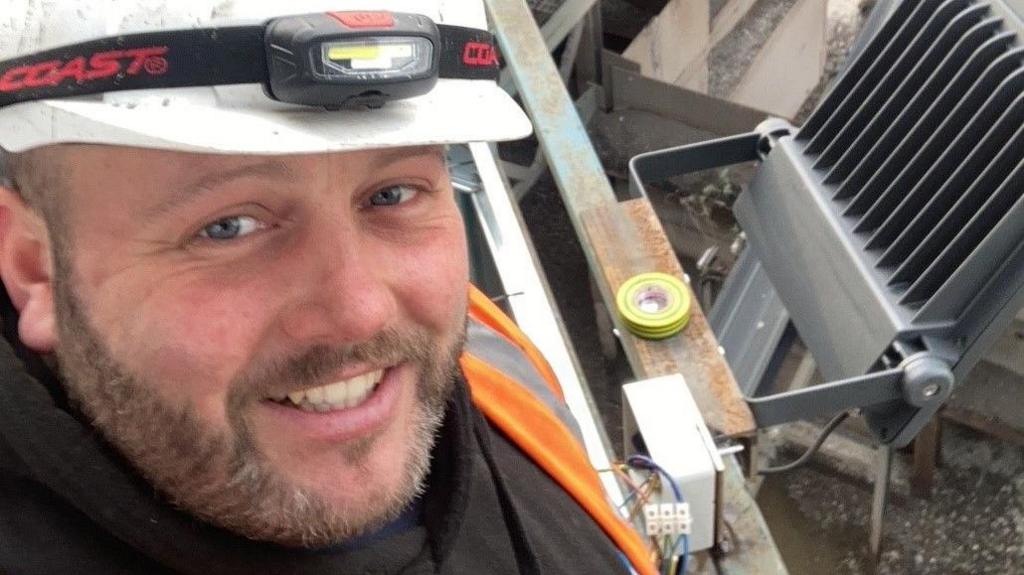 Oliver Powell wearing a white hard hat and orange hi-vis while smiling into the camera.