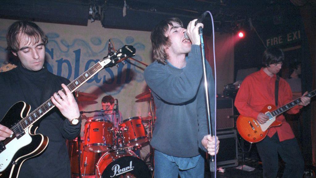 Oasis performing at The Water Rats in 1994. Bonehead and Noel Gallagher are on guitars. Liam Gallagher is singing and holding his microphone