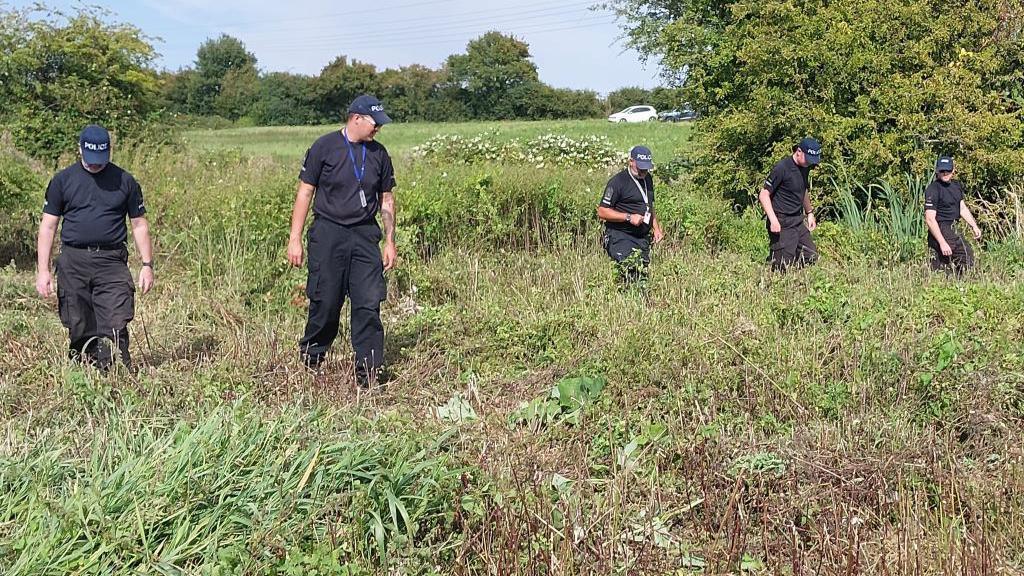 Several police officers wearing all black walking in a field.