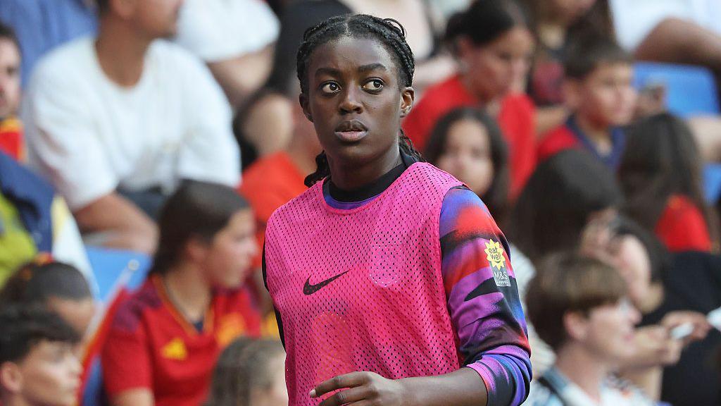 Michelle Agyemang walks along pitch side wearing a pink bib