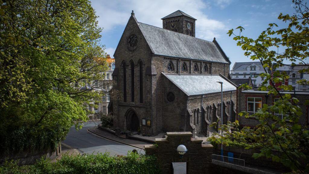 The exterior of St Thomas' Church, the brown brick building is on the corner of a street.