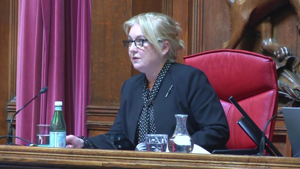 Judge speaking while sitting on red chair behind long wooden bench