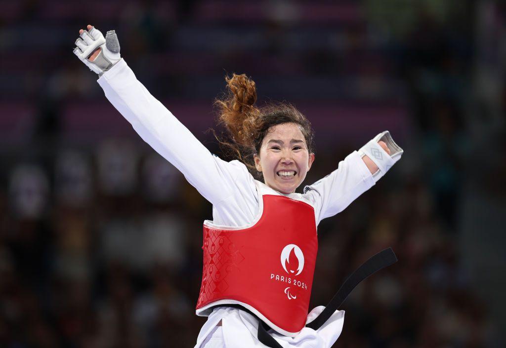 zakia smiles and appears to jump for joy with her arms in the air dressed in her taekwondo gear