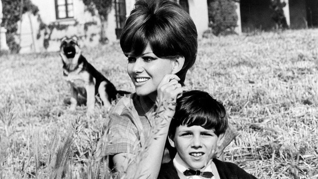 Claudia, who has a voluminous cropped haircut, rests her hand on her young son's Patrick head, as they are pictured sitting in a cornfield. An Alsatian dog is seen sitting in the background