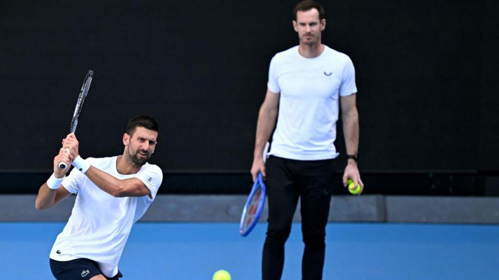 Novak Djokovic hits the ball as Andy Murray watches 