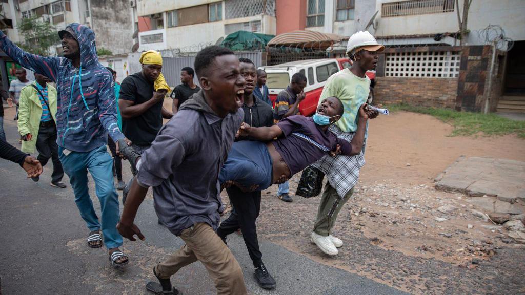 A group of male protesters carry another protester injured by a rubber bullet fired by riot police in Maputo