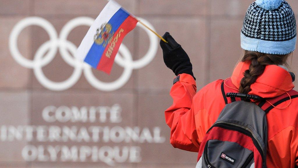 A supporter waves a Russian flag in front of the logo of the International Olympic Committee