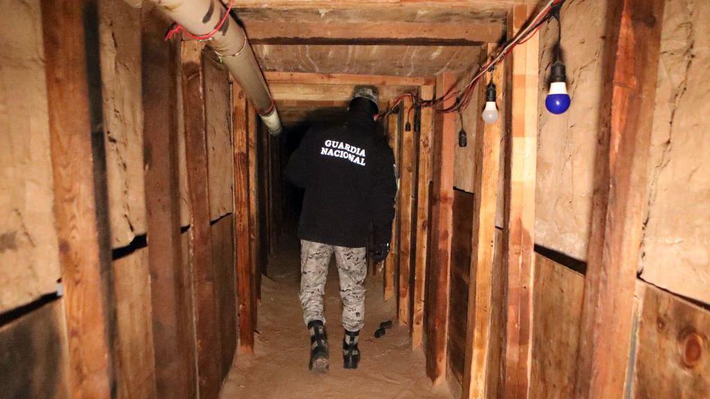 A national guard agent, with his back to the camera, inspects a tunnel reinforced by wooden beams