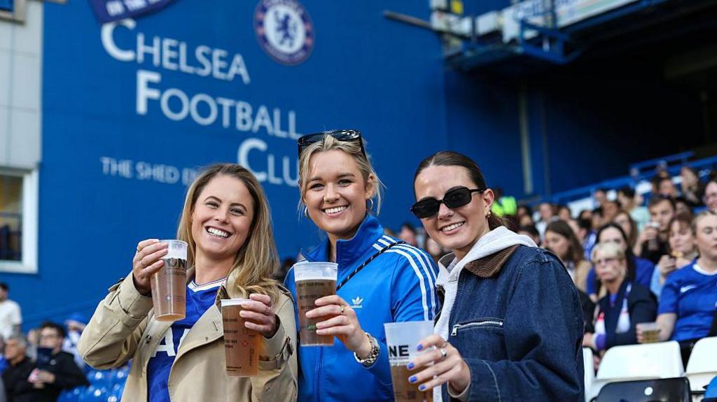 Fans enjoy pints of beer in the stands at Stamford Bridge during the WSL game against Manchester City
