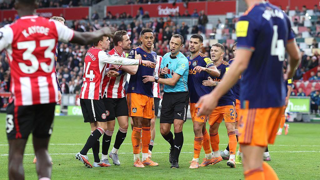Players surround referee Stuart Attwell as he shows a yellow card to Dango Ouattara