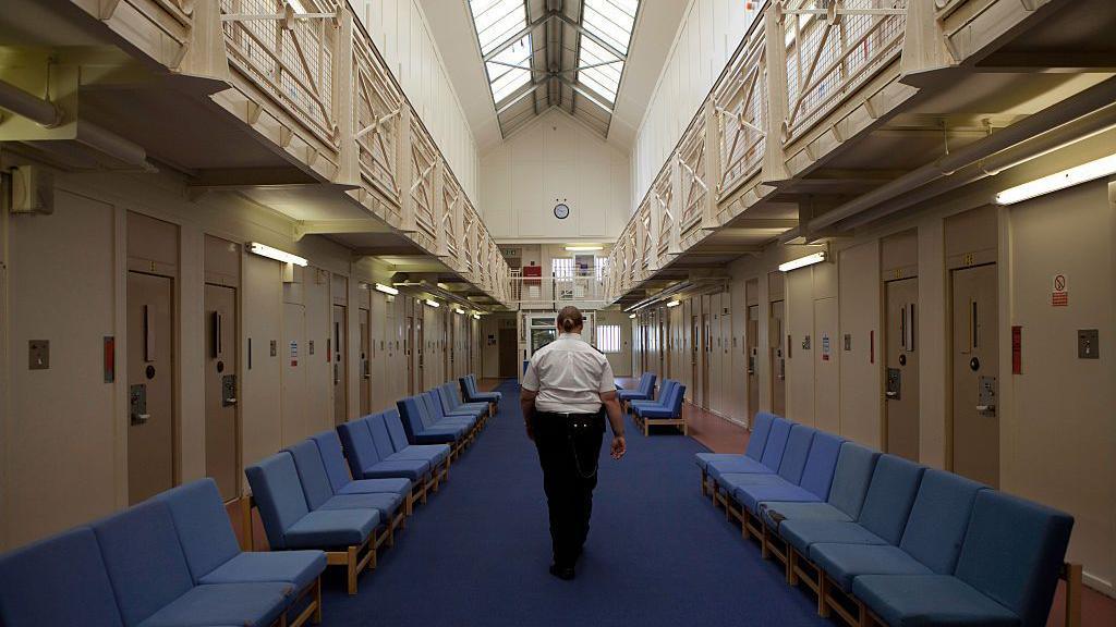 Archive image of the interior of HMP Styal. A prison officer walks away from the camera down the prison wing.