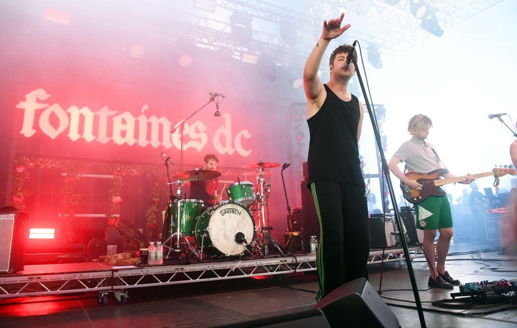 Grian Chatten and Conor Deegan from Fontaines DC perform at Way Out West Festival in Slottskogen on August 12, 2022 in Gothenburg, Sweden.
They are wearing black and green outfits, with a red lit up Fontaines DC sign visible behind a man playing the drums.