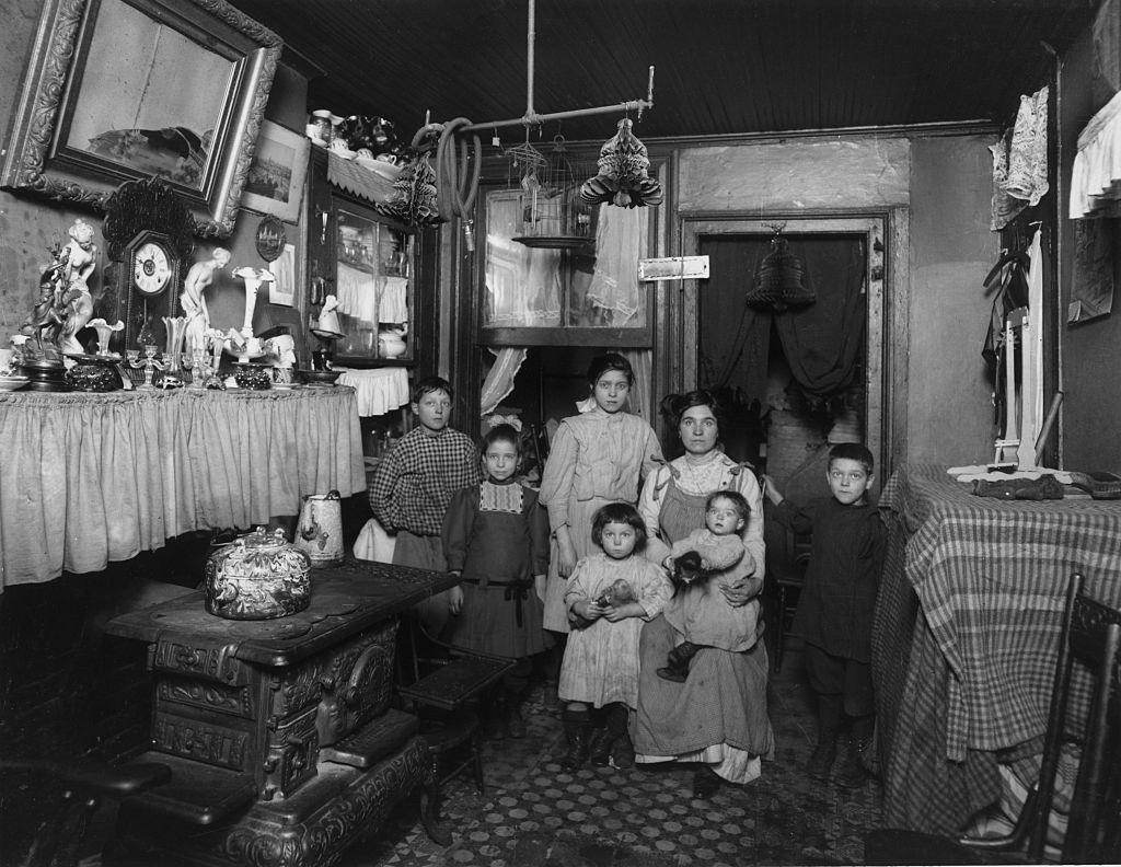 Black and white photo of Immigrant family in New York City. Mother is seated holding baby on her lap