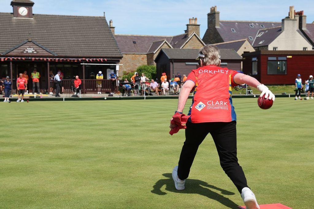 Women rolling lawn bowl across the green, wearing a red tshirt