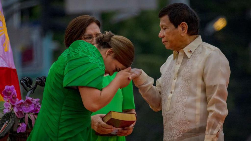 Sara Duterte greets her father, Philippine President Rodrigo Duterte, after taking her oath as the next Vice-President by touching his hand to her forehead. Her mother watches standing next to her.