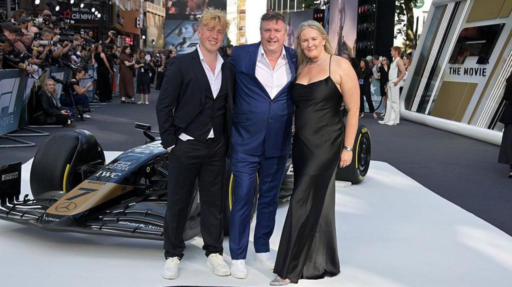 David Croft is wearing a navy suit and stood in front of an F1 car at the F1 premiere.