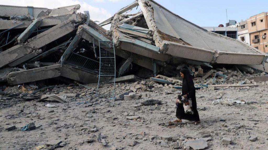 A Palestinian woman carries belongings as she walks amid debris at a United Nations school where displaced people were taking shelter, after it was hit in overnight Israeli strikes, amid an Israeli military operation, at Zeitoun neighbourhood in Gaza City, October 1