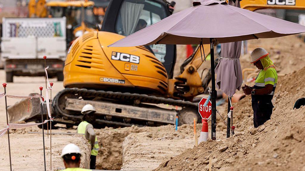 A worker shelters under an umbrella on a building site in Madrid