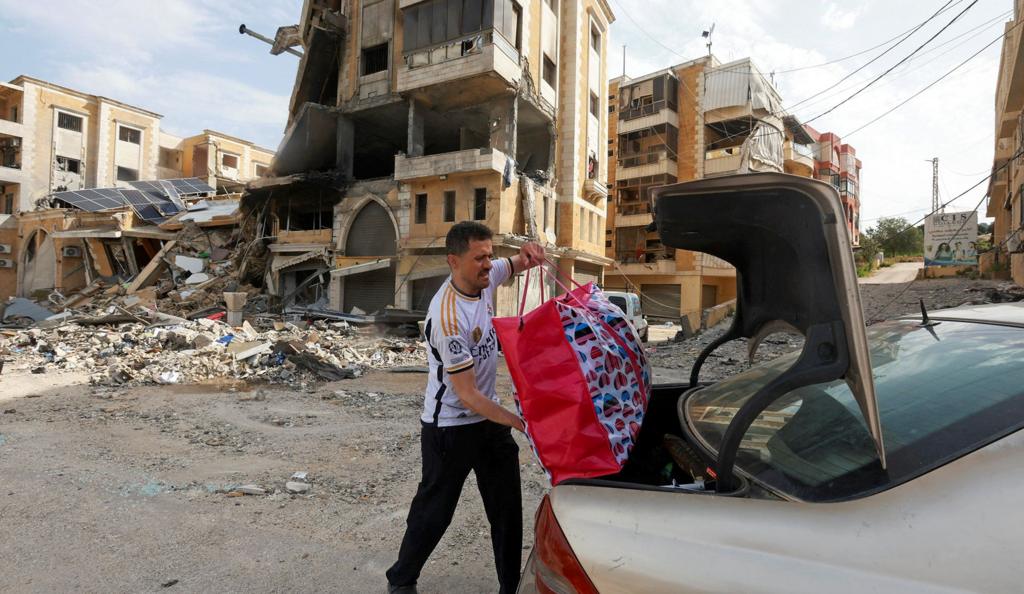 A person loads a bag of belongings into the boot of a car in front of a damaged building in Nabatieh