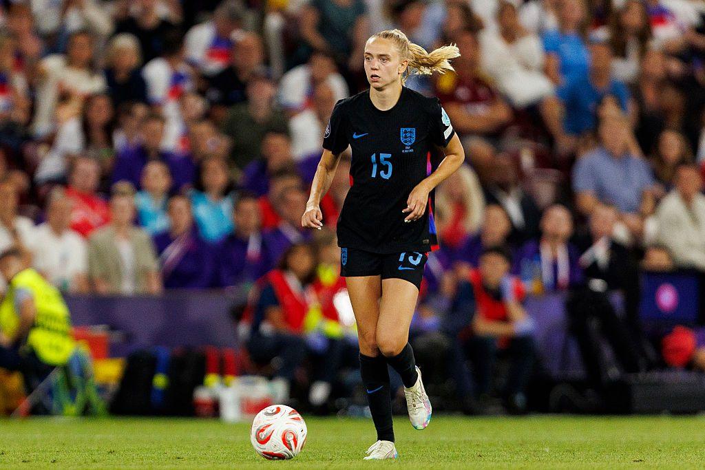 Esme Morgan dribbles for England. Wearing an all-black kit with blue detail, Morgan has long blonde hair.