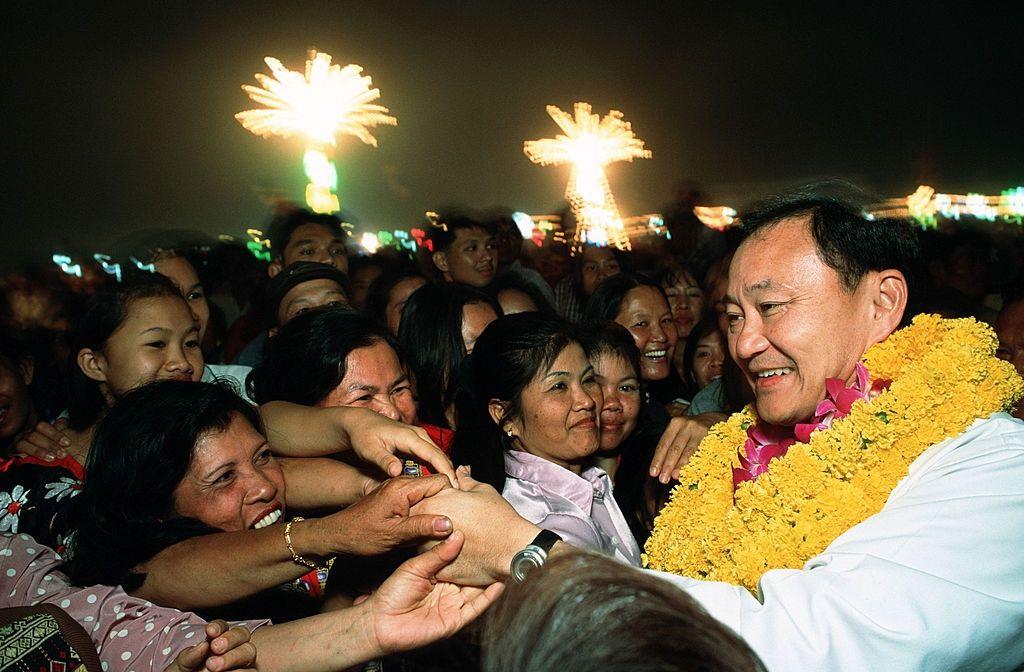 A younger Thaksin wearing a garland of yellow marigolds and pink orchids greets a crowd of supporters at a night rally
