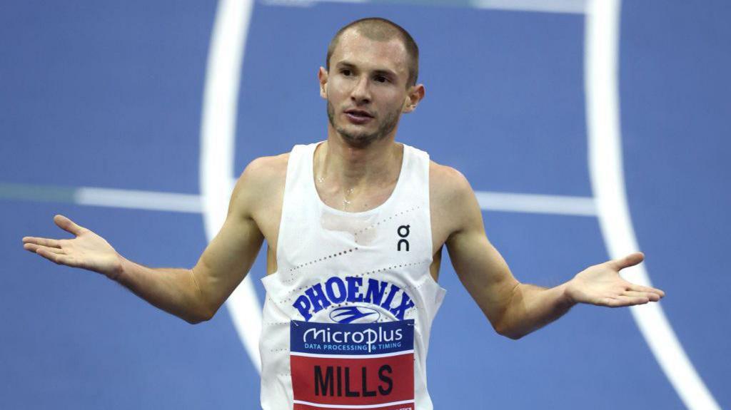 George Mills gestures with open palms at the end of a race