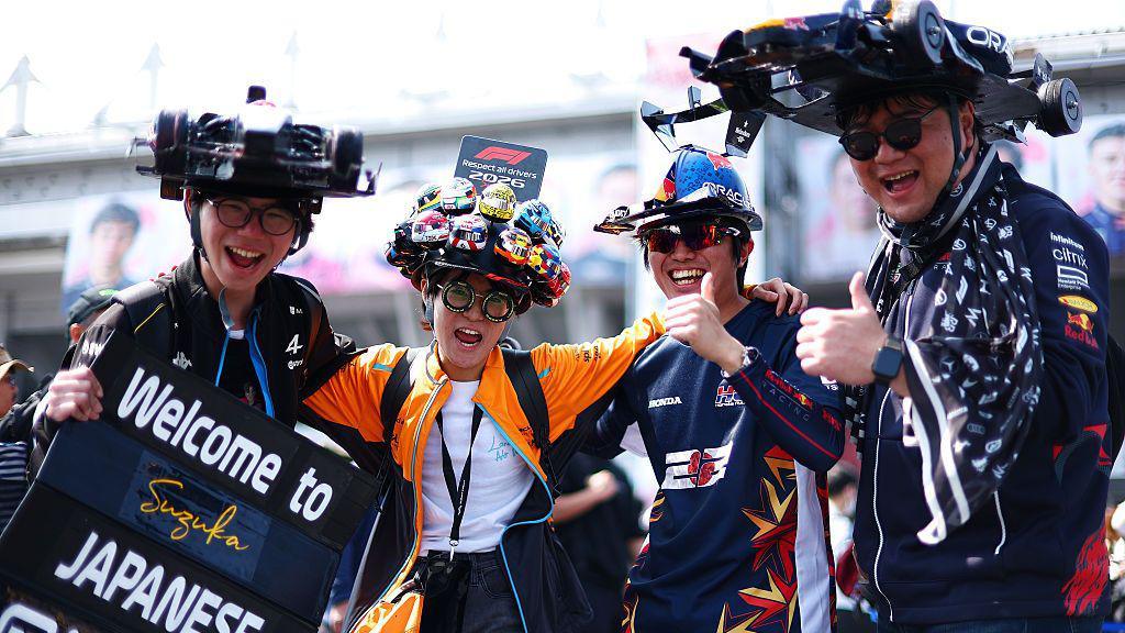 Fans wear hats designed like cars and give a thumbs up in the fanzone at Suzuka 