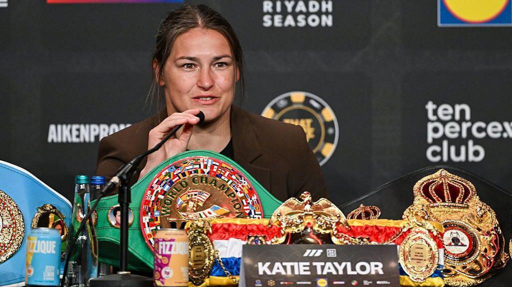 Katie Taylor speaks into a microphone and has the WBC and IBF 