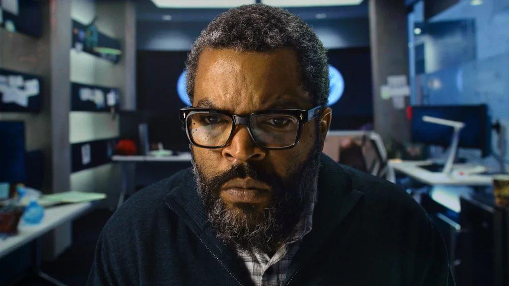 Ice Cube in an office facing the camera and staring intently at a screen