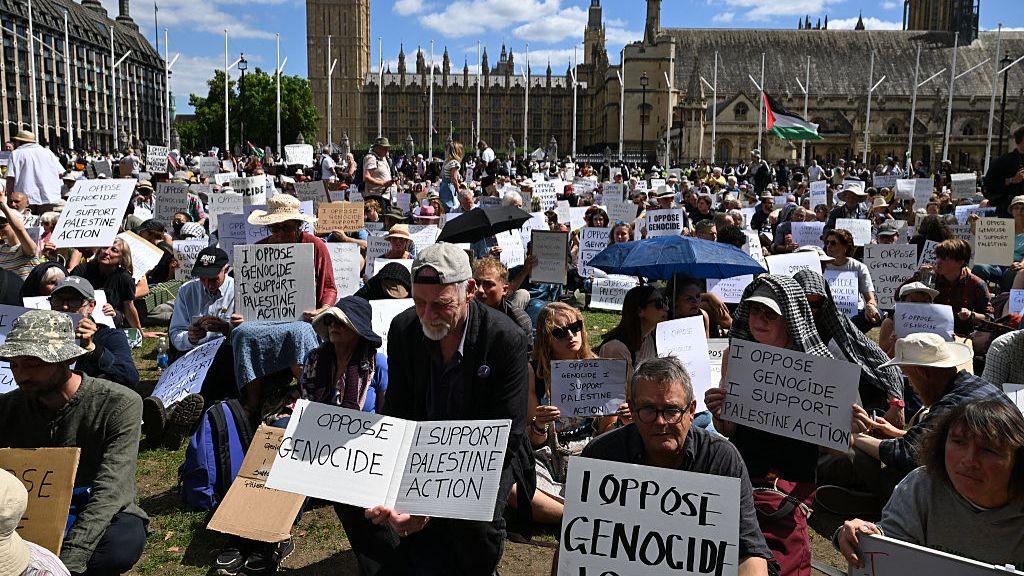 Protesters sit with placards supporting of Palestine Action at a demonstration in Parliament Square.