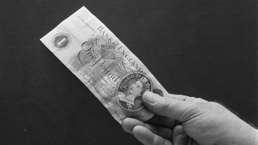 A black and white photo of someone holding a one pound note