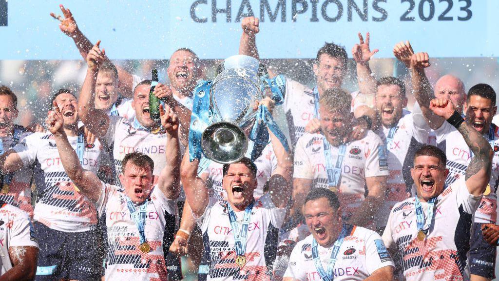 Owen Farrell lifts the European Champions Cup, surrounded by team-mates jumping up and down while spraying champagne