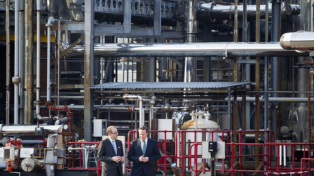 David Cameron (right) talks with CEO of GlaxoSmithKline, Andrew Witty, during a visit to the Ulverston site. They are both wearing dark suits. Mr Cameron has dark hair while Mr Witty has fair hair and glasses.