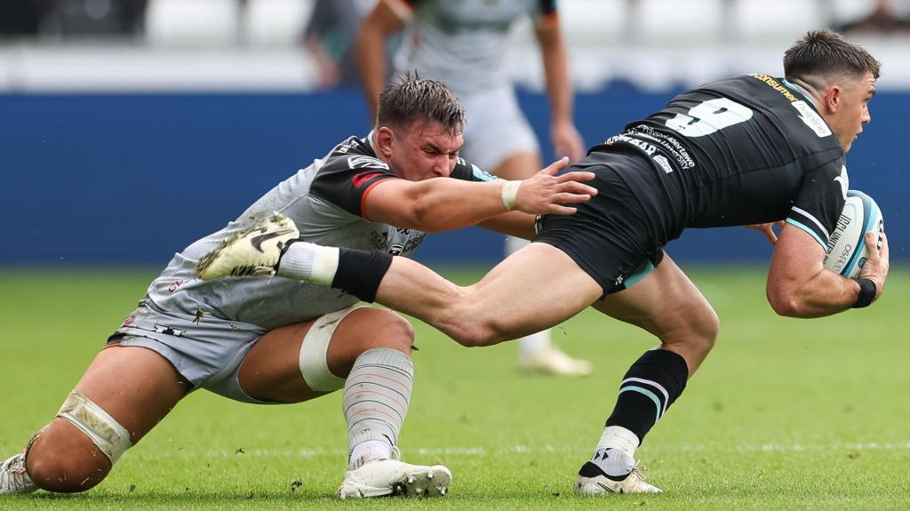 Reuben Morgan-Williams of Ospreys is held by Taine Basham of Dragons