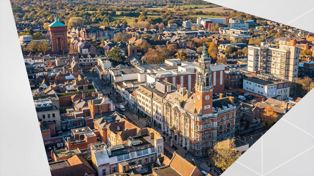 An aerial viewpoint of a Colchester town centre, with a series of red-brick buildings and a clock tower in centre frame. 