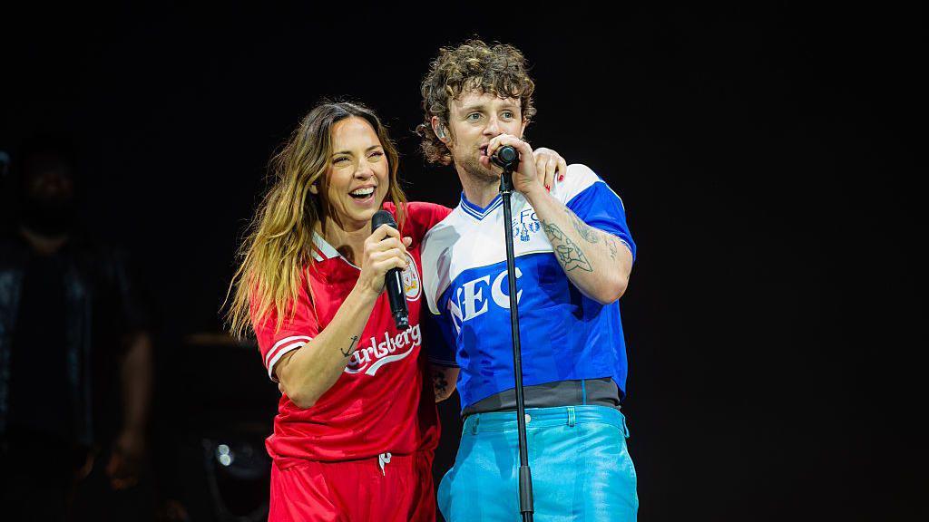 Mel C with Tom Grennan on stage, both are holding microphones.