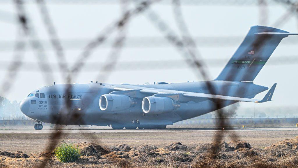 A C-17 Globemaster III aircraft, a large military transport plane with four engines and "US Air Force" written on the side behind the cockpit - it is pictured through coils of barbed wire fencing at Sri Guru Ram Dass Jee International Airport in Amritsar.