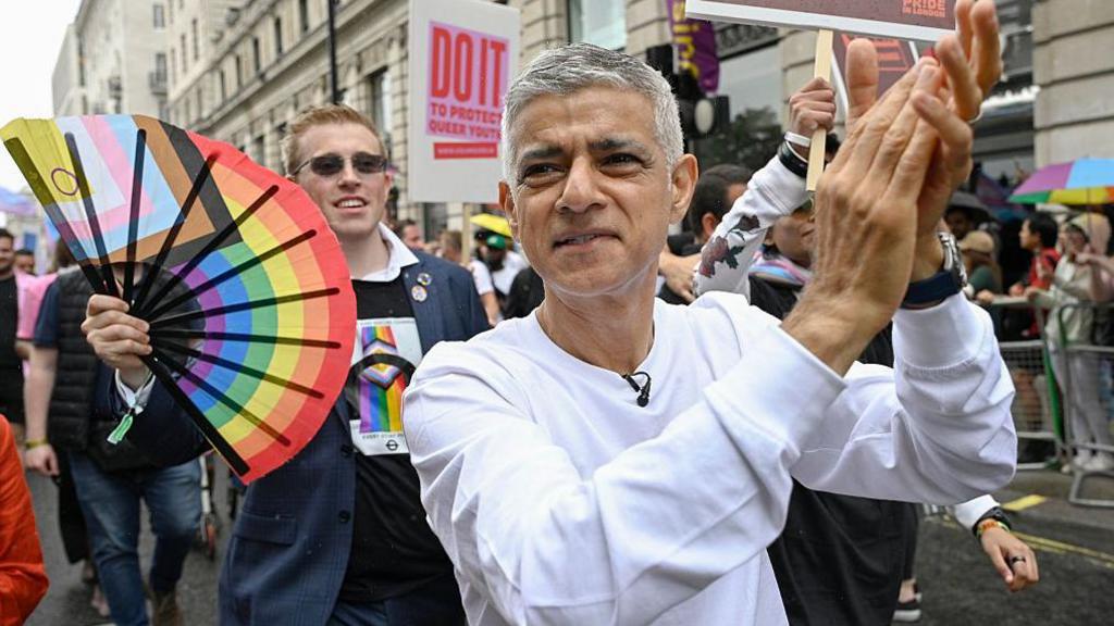 The mayor in a white jumper claps his hands together as he takes part in the parade. 