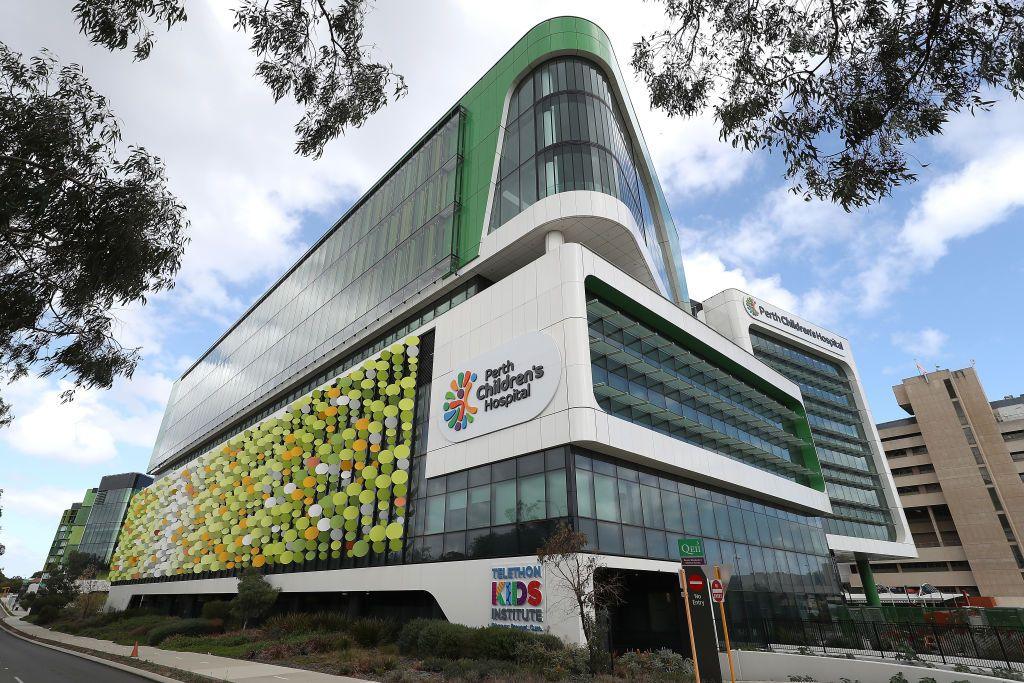 A bright modern hospital building viewed through a gap in trees