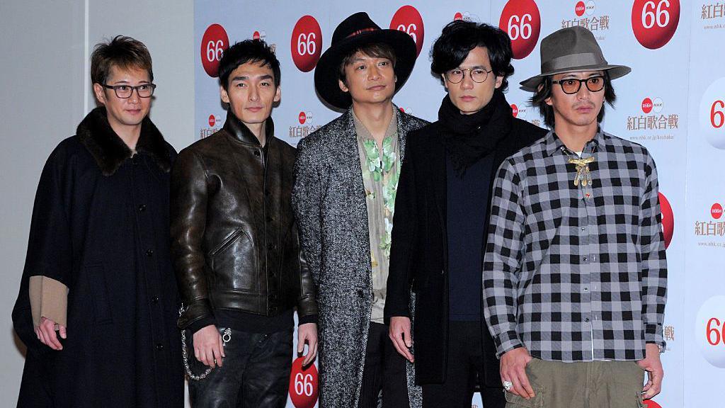 The members of SMAP standing in a row and posing for photos at an event, mostly wearing black outfits. 