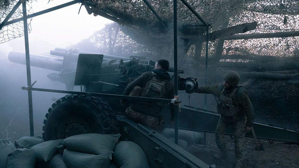 Ukrainian artillerymen fire a gun in a foggy sky underneath netting near Pokrovsk