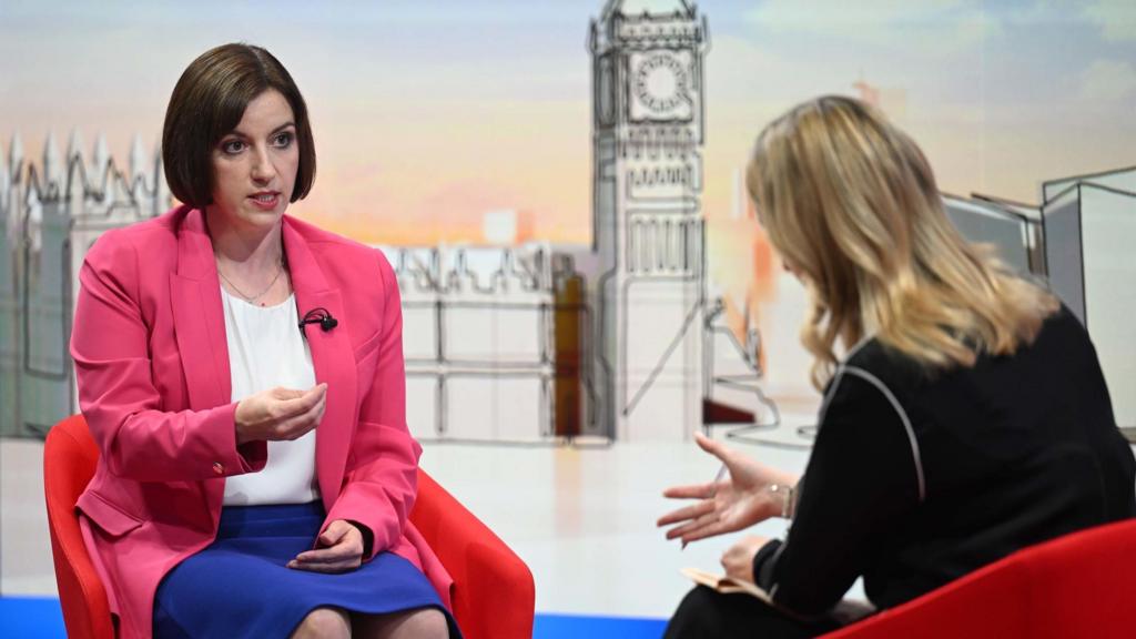 Bridget Phillipson (L) answers questions in a hot pink blazer, white shirt and blue skirt while sitting on a red chair. In front of her, with her back to the camera, is Laura Kuenssberg in a black ensemble