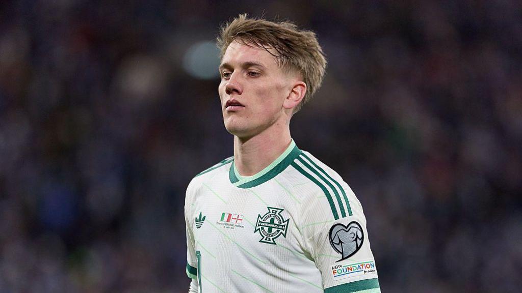 Ethan Galbraith in action for Northern Ireland. He is wearing a white and dark green trimmed away shirt.