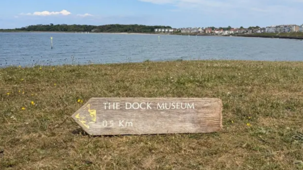 The wooden sign which is a shape of an arrow with The Dock Museum and 0.5Km written on it.