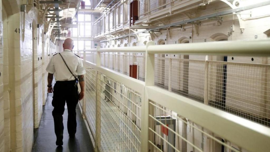 A prison officer walks along a prison walkway 