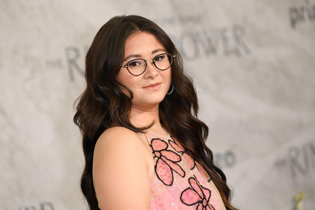 Megan Richards attends "The Lord of the Rings: The Rings of Power" World Premiere. In the head and shoulders shot she is wearing glasses and a pink dress